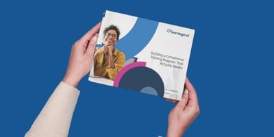 Person holding a Learning Pool booklet titled 'Building a Compliance Training Program That Actually Works' against a solid blue background.