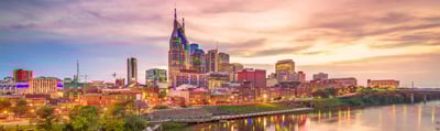 Panoramic view of downtown Nashville at sunset, featuring the iconic AT&T building, illuminated city lights, and reflections on the Cumberland River.