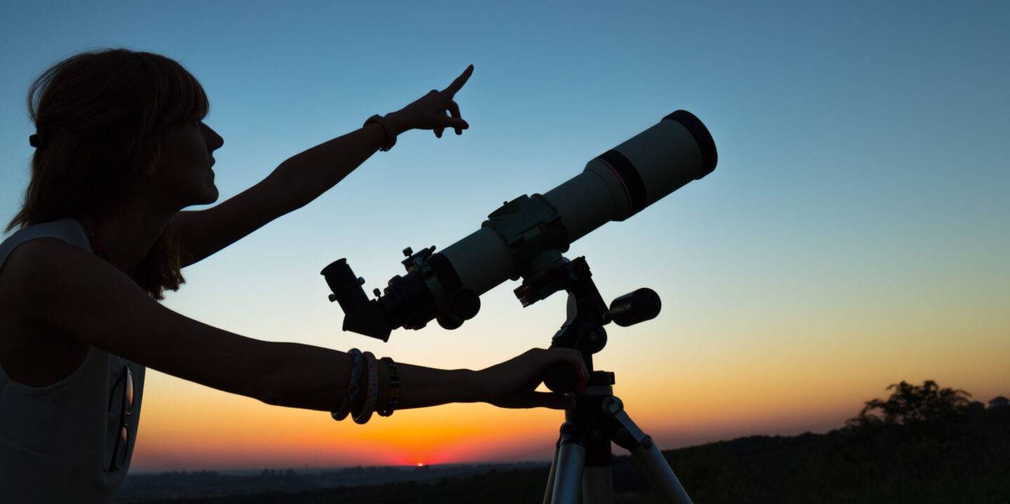 person pointing while using a telescope